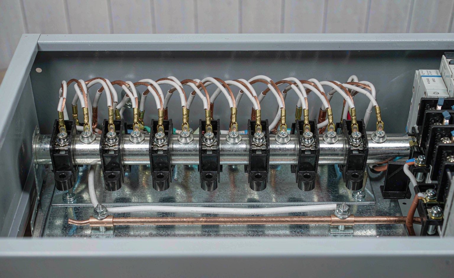 Annotated view inside a residential load center showing the neutral bar with white conductors, its insulating standoffs above the panel backplane, and the separate bonded ground bar at the bottom